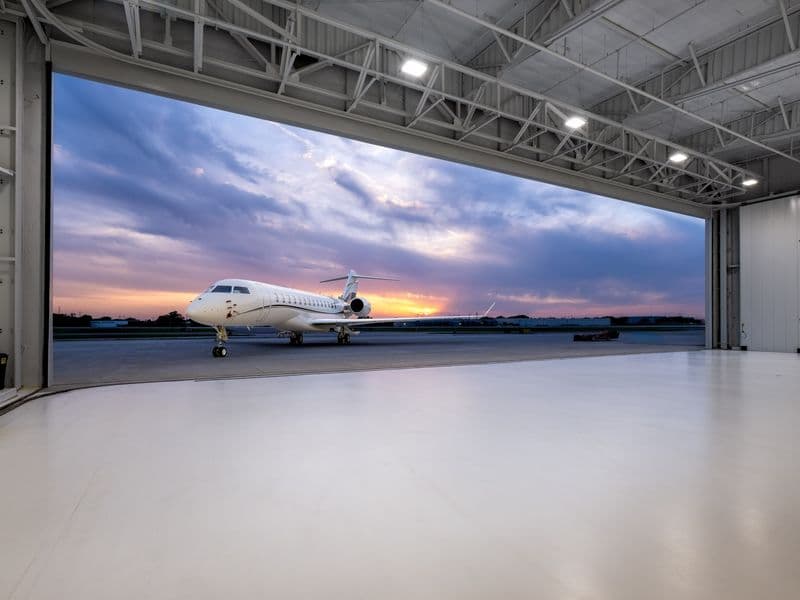An empty business jet hangar at dusk with a Global on the ramp beyond